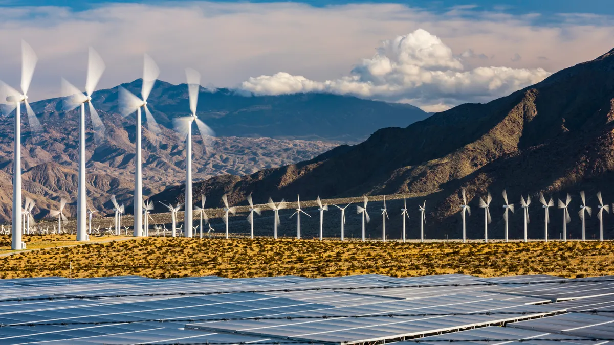Wind turbines spin with solar panels in the foreground.