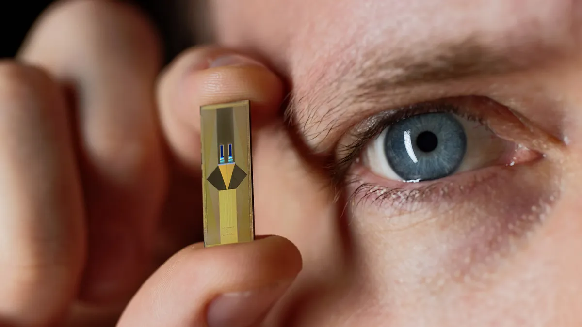 A person holds SteerLight's compact lidar-on-a-chip next to their right eye to show its compact size.