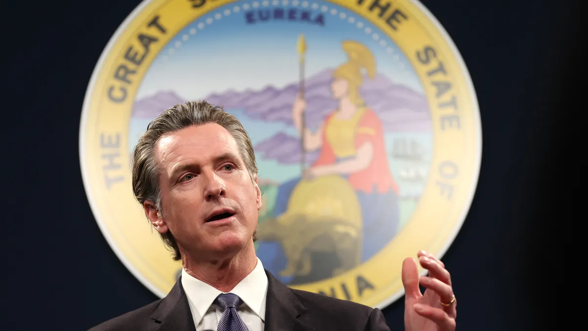 California Gov. Gavin Newsom speaks into a microphone with the seal of California behind him