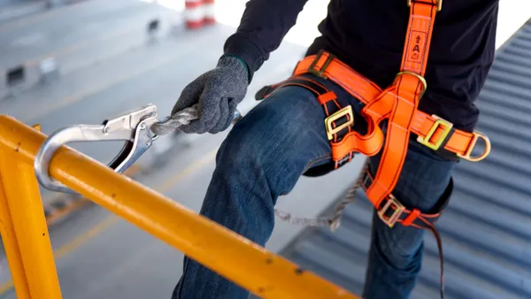 A construction worker with a safety harness tied to a metal railing.