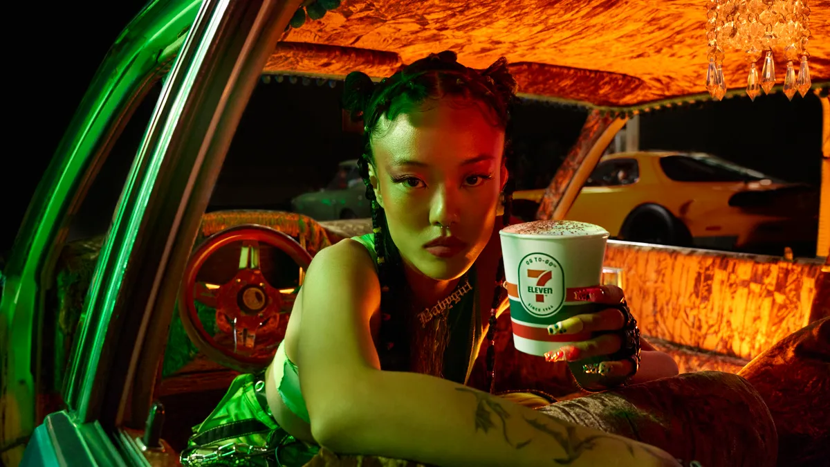 A photo of a person in a car, holding a 7-Eleven coffee and looking at the camera.