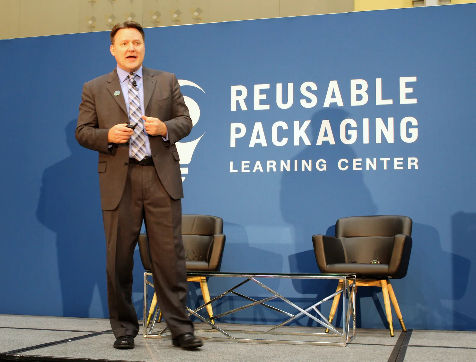 A person speaks from a stage in front of a background that says Reusable Packaging Learning Center.