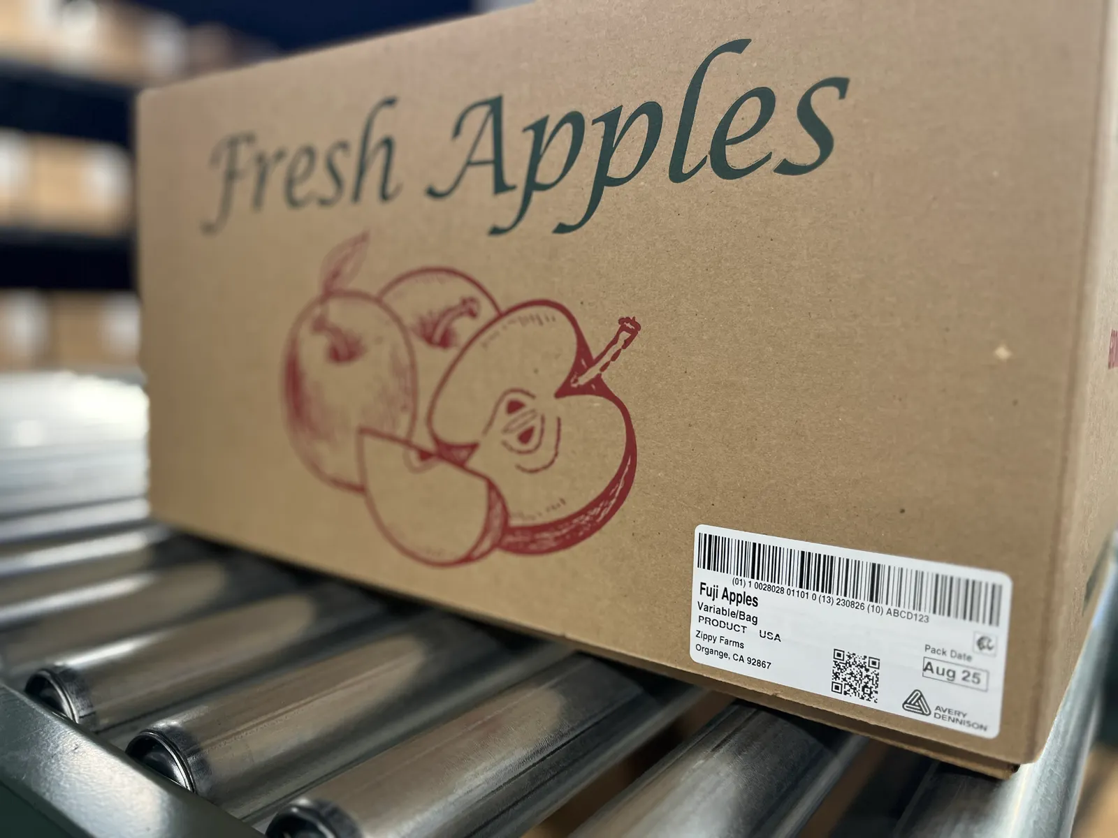 A brown cardboard box labeled apples with a white tag on the outside describing the contents of the box.