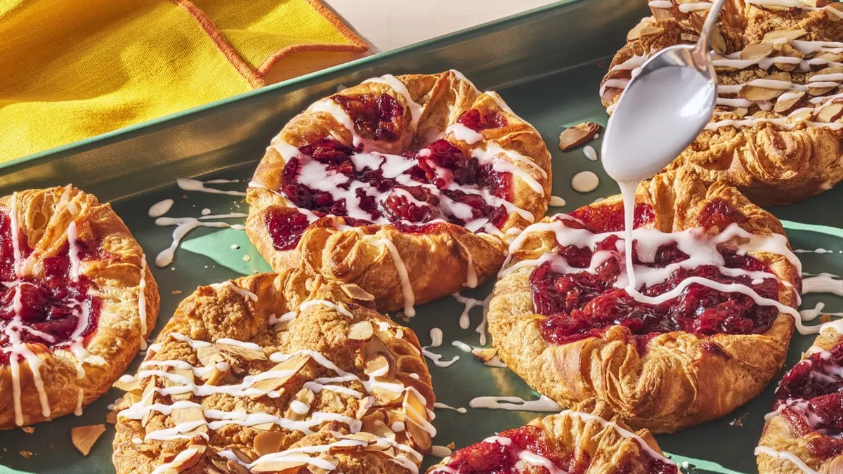 An image of several cherry and almond pastries with a spoon drizzling icing on top.