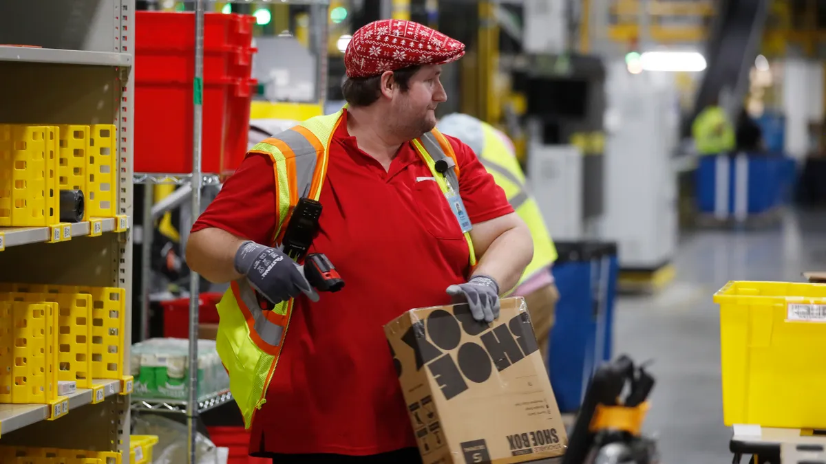 An Amazon warehouse employee wearing a festive hat scans a package.