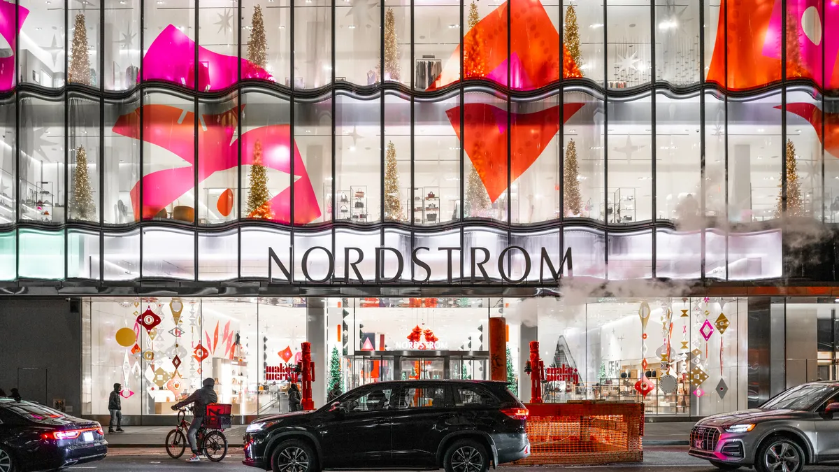 Christmas trees and huge bright pink and orange graphics decorate the outside of a Nordstrom store.