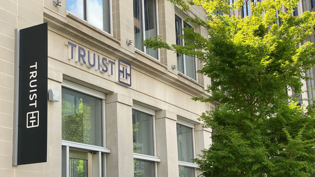 The Truist name is shown vertically and horizontally on a building facade with tree branches on the right side of the frame