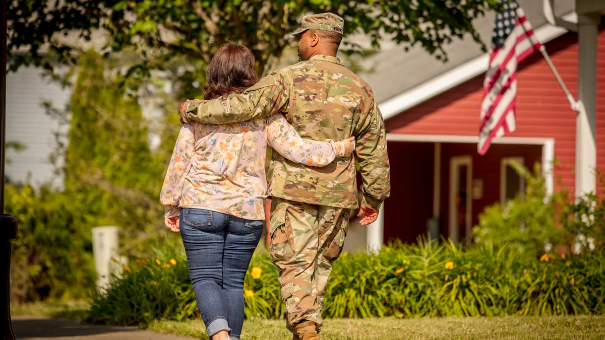 A couple, one of them in camo, walk through a neighborhood.