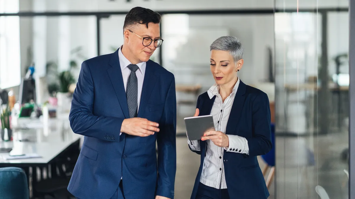 A CEO and chief compliance officer have a discussion in an office hallway