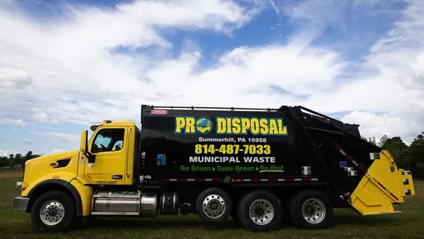 A yellow Pro Disposal truck is parked in a field