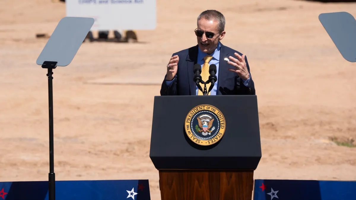 Executive Pat Gelsinger speaks at a lectern bearing the seal of the president in front of a construction worksite