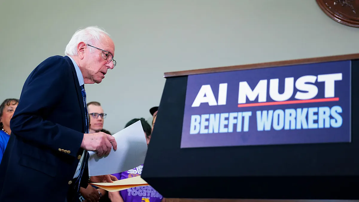 Bernie Sanders stands in front of a sign that says "AI MUST BENEFIT WORKERS."