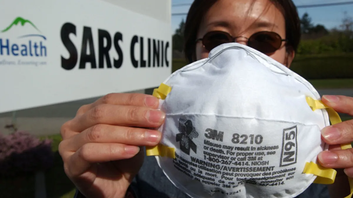 A person holds up an N95 mask in front of a sign that says "SARS Clinic"