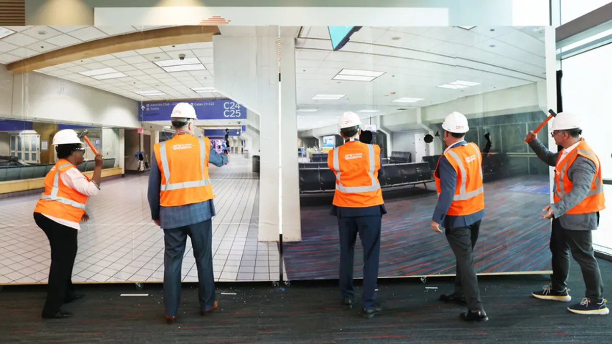 Five people in white hard hats and orange reflective vests stand with hammers in front of a large photo of the new Terminal C.