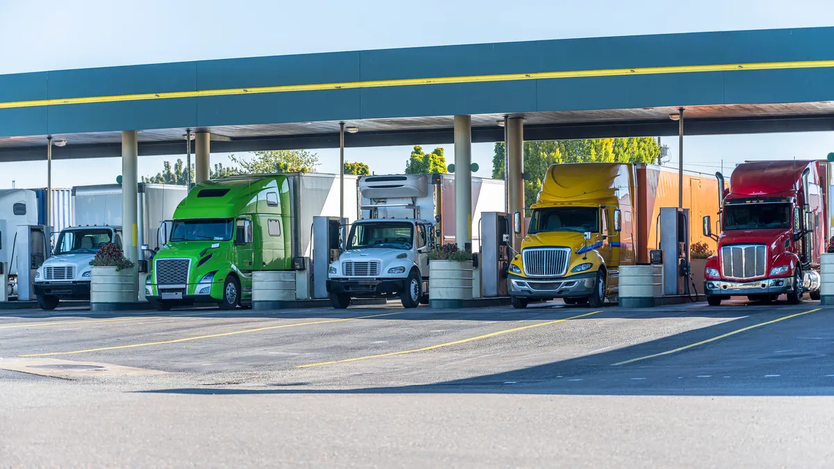 Differently sized trucks under the awning of a gas station pumps area.