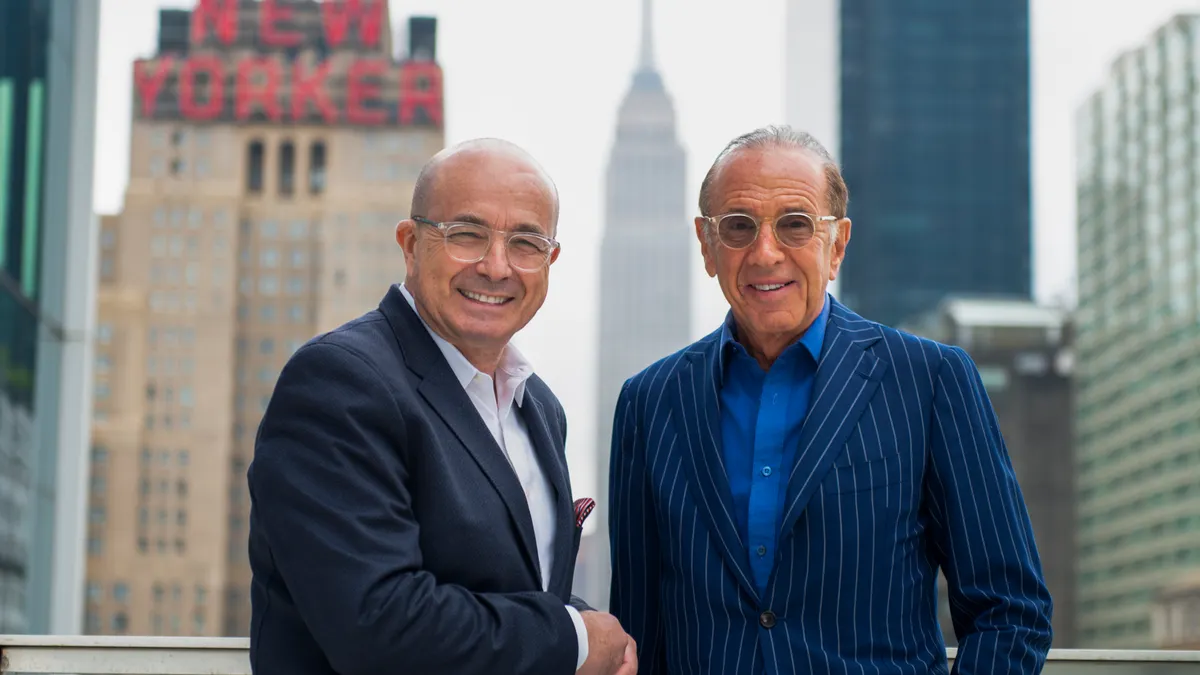 Two men shake hands and face the camera, with skyscrapers in the background
