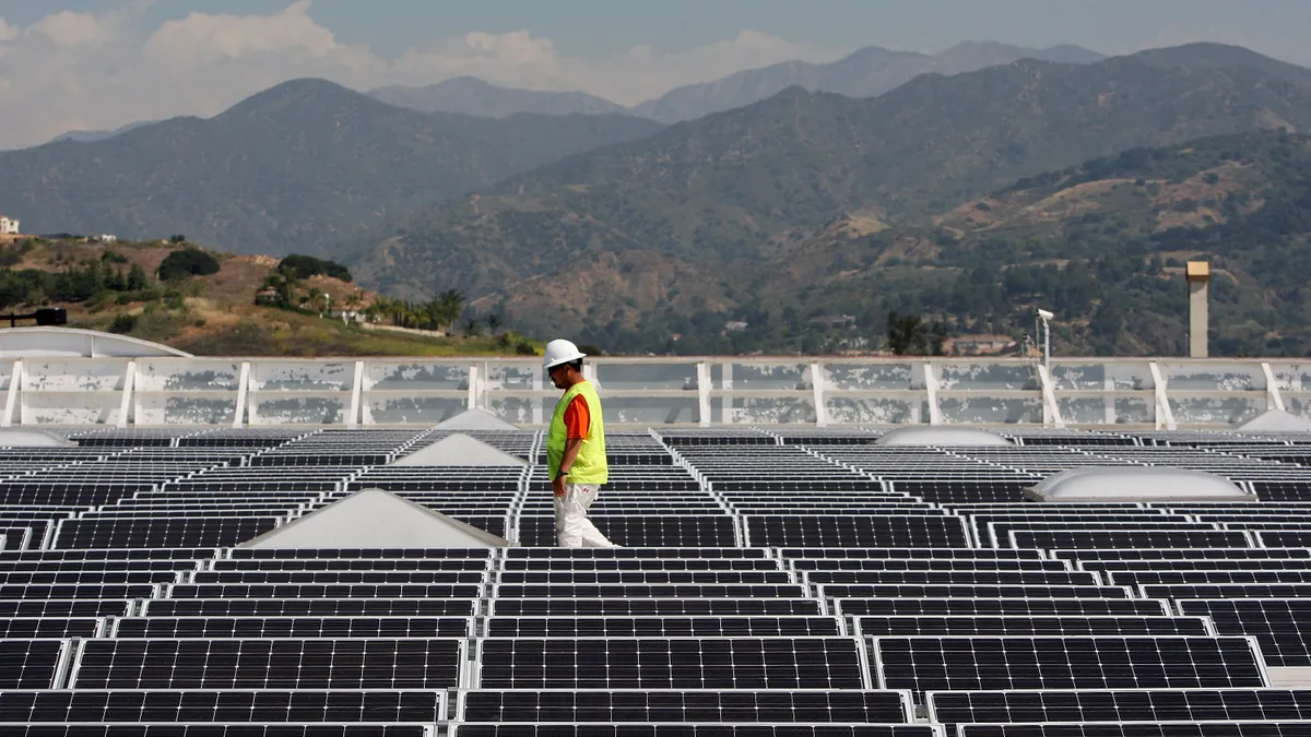 A worker in a high-vis vest and hard hat walks between solar panels that cover the roof of a Sam's Club store in California.