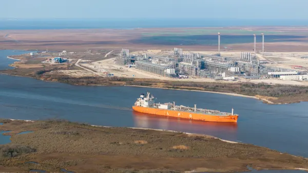 A ship moves through a waterway near an industrial facility.