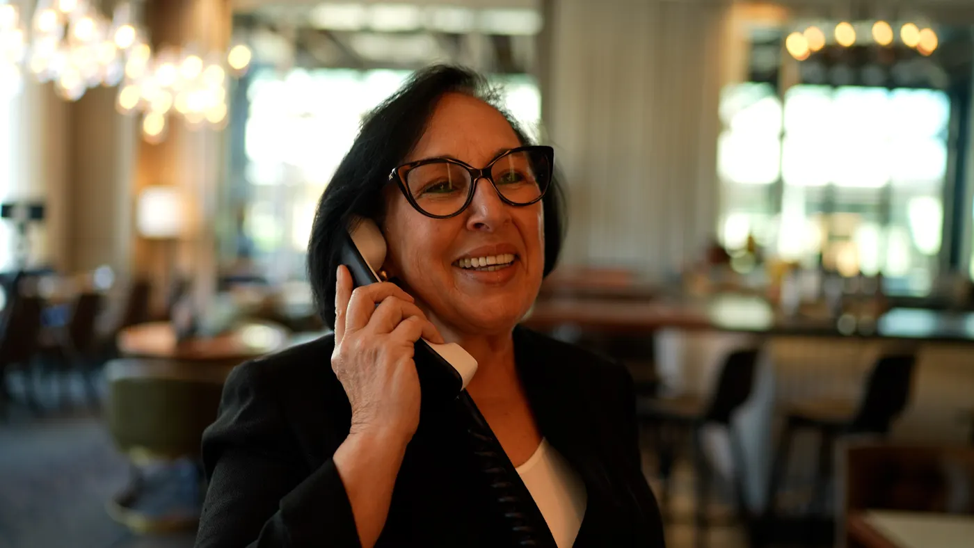 An image of a person wearing a black blazer and holding a phone up.
