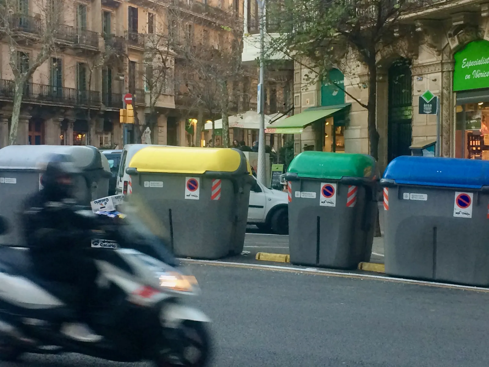 Multiple shared waste containers on a street in Barcelona, with a motorbike in foreground