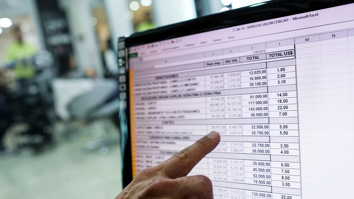 A person points to a spreadsheet on a computer screen.