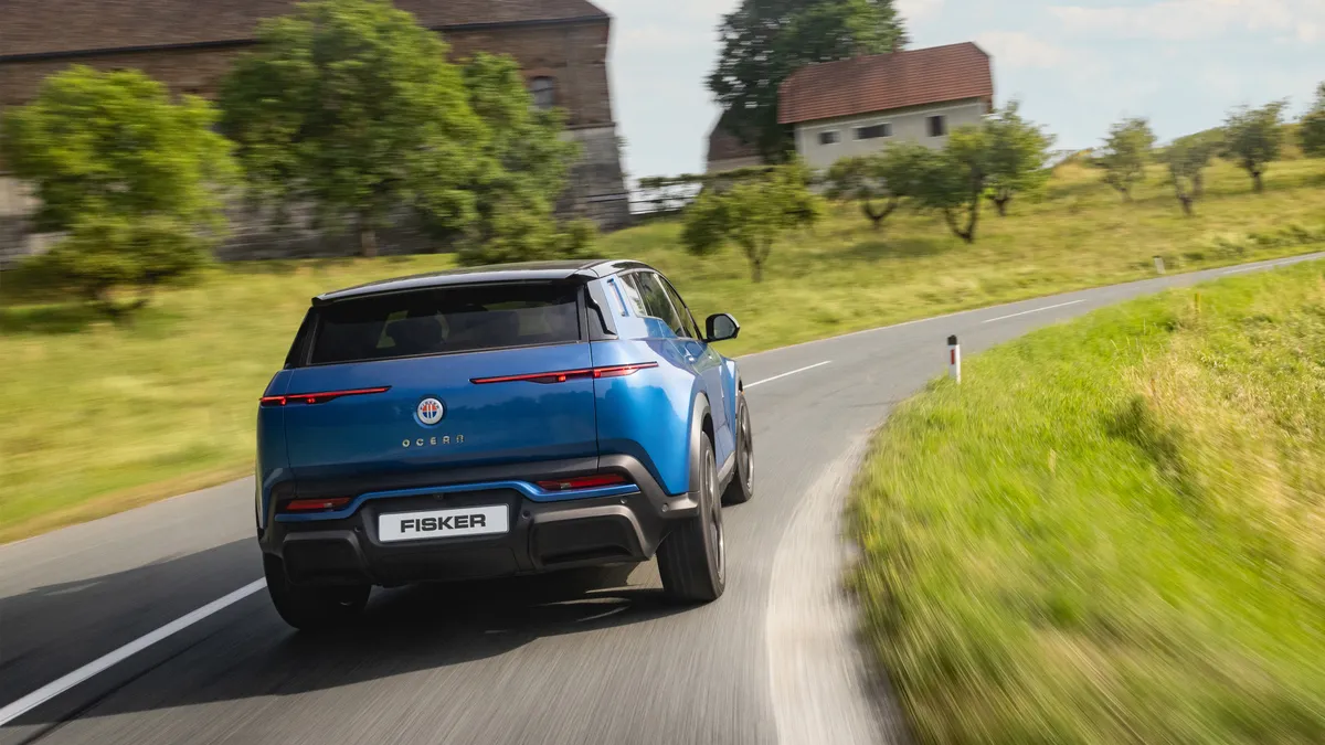 A 2024 Fisker Ocean driving around a bend on a rural road.