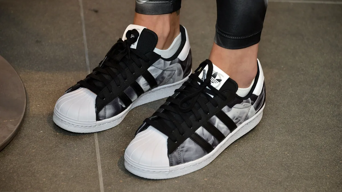 A close-up of a person's feet wearing Adidas sneakers in black, white and grey.