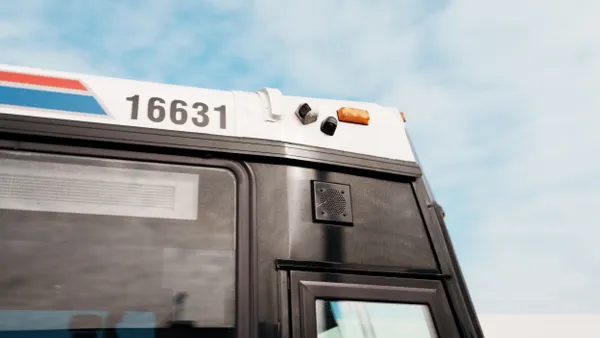 View looking up toward the right-side front of a large bus, with two small cameras mounted above the front door.