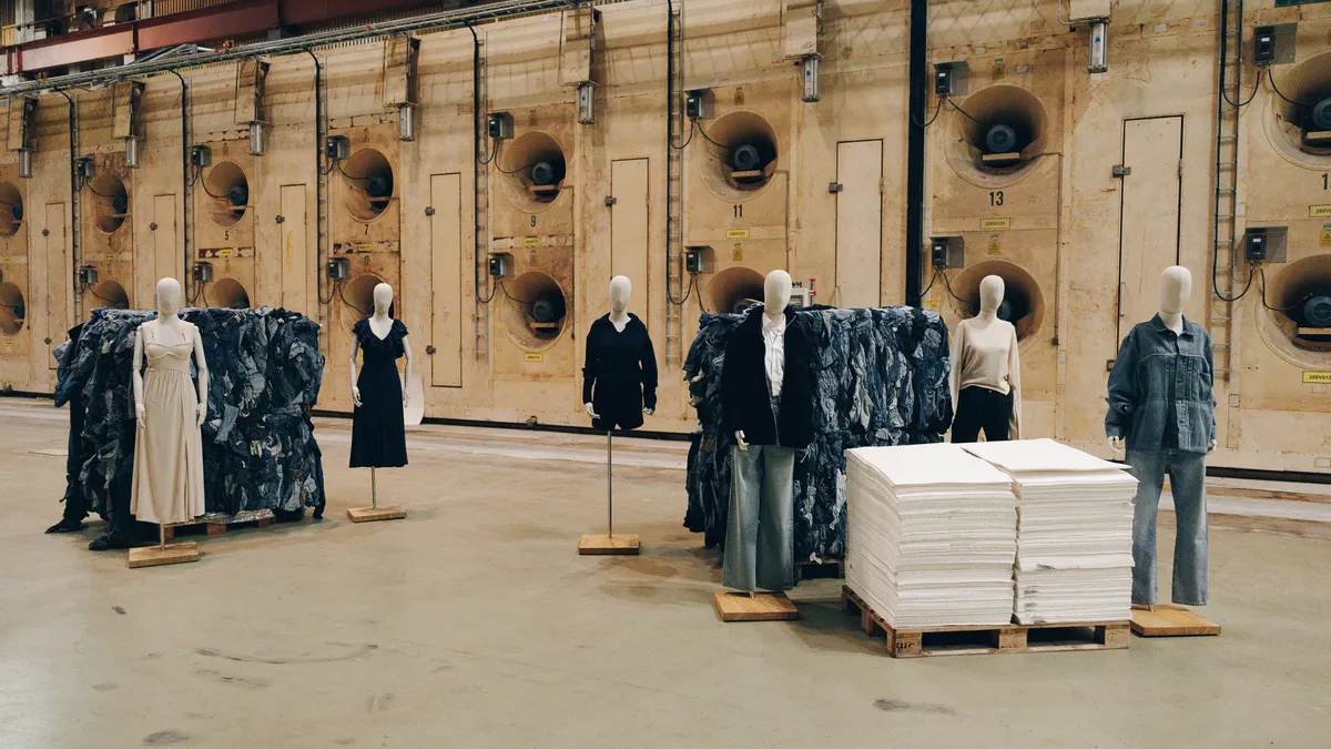 Mannequins stand in a warehouse dressed in neutral colors and denim, next to stacks of material.