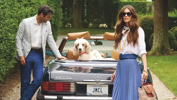 Two people stand by a convertible car with a dog inside.