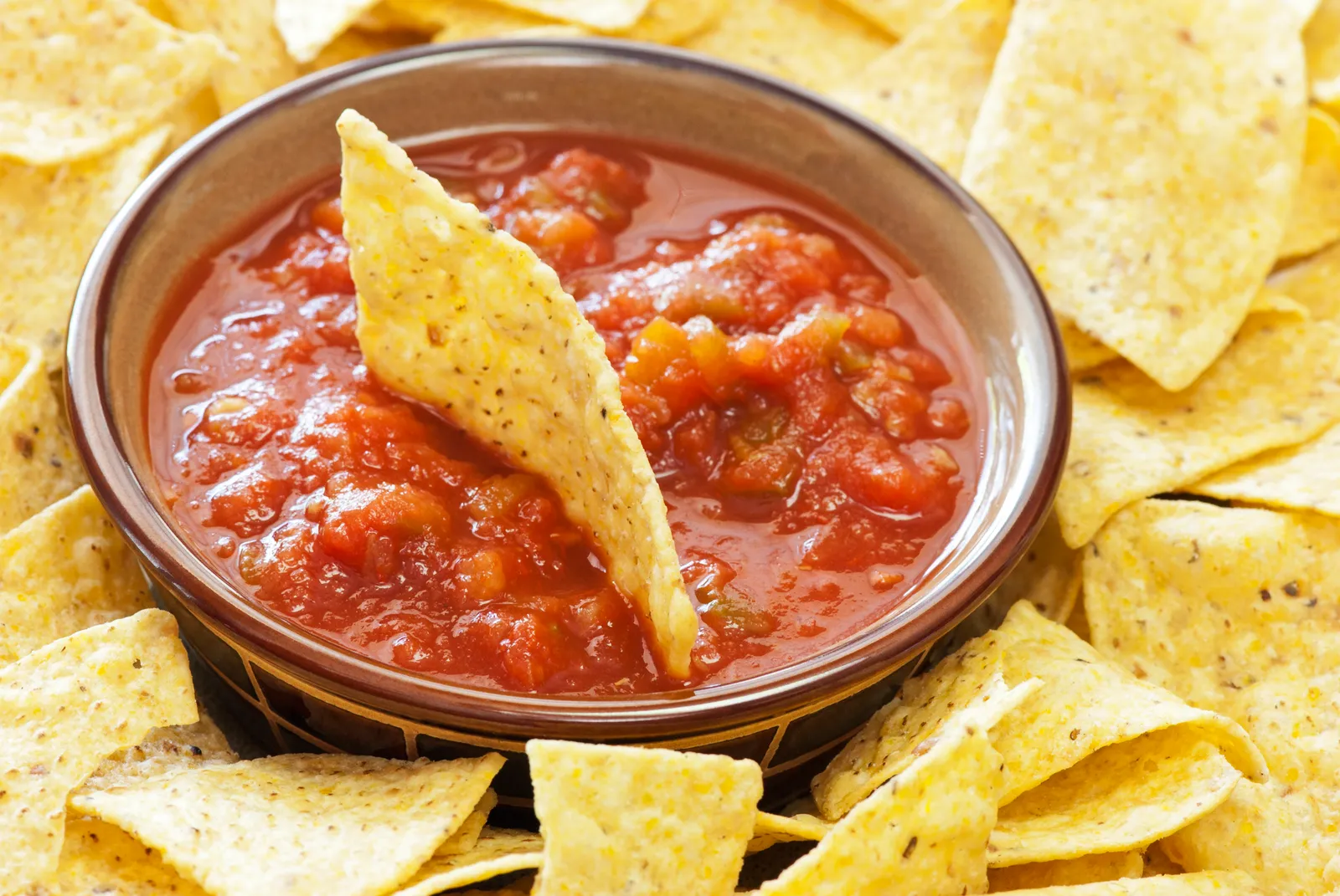 A photo of tortilla chips arranged around a bowl of red salsa.