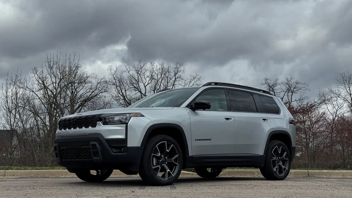 A grey 2026 Jeep Cherokee Overland sits on a parking lot with a stormy sky in the background.