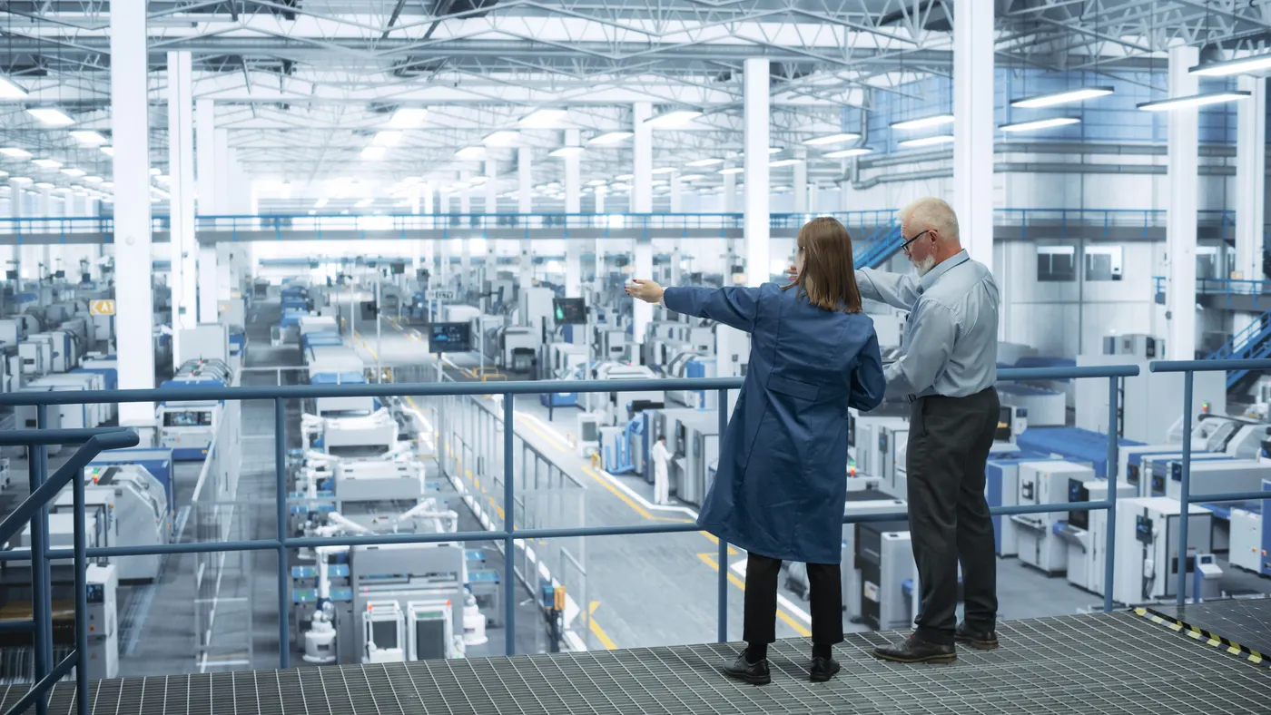 Engineers stand on a platform looking out at a factory.
