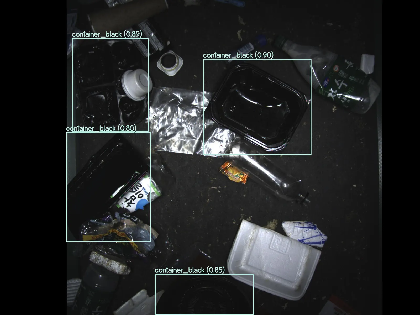 A computer screen shows an image of packaging items on a conveyor for sorting, with three black plastic items labeled in digital boxes.