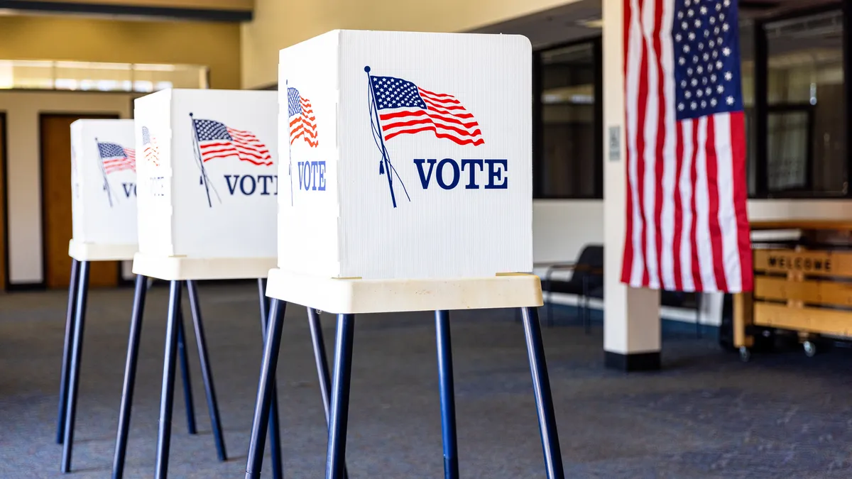 Three white booths inscribed with the word "vote" and an American flag.