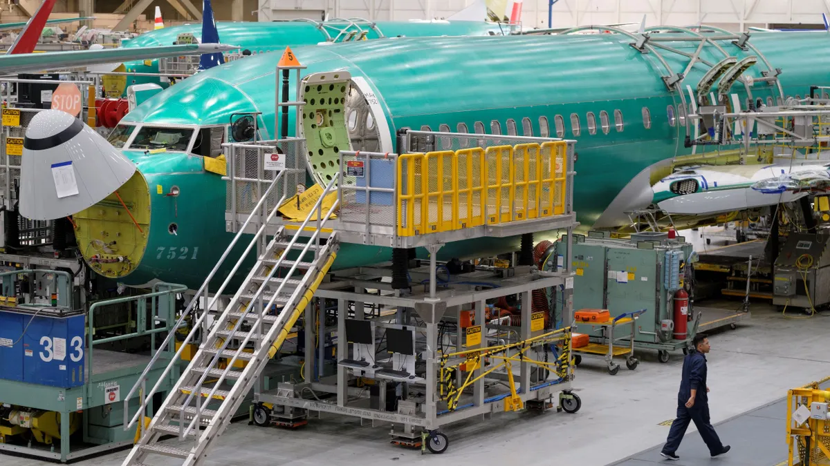 An employee walks past a teal plane at a factory.