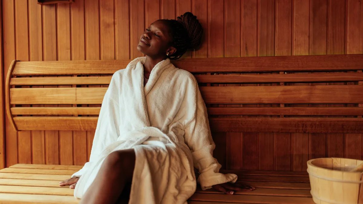 A woman in a white robe sits in a sauna.