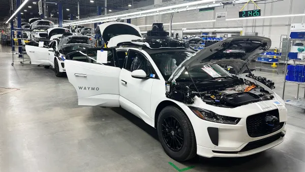 A group of Jaguar I-PACE SUVs painted white in the general assembly area of the robotaxi facility in Mesa, Arizona.