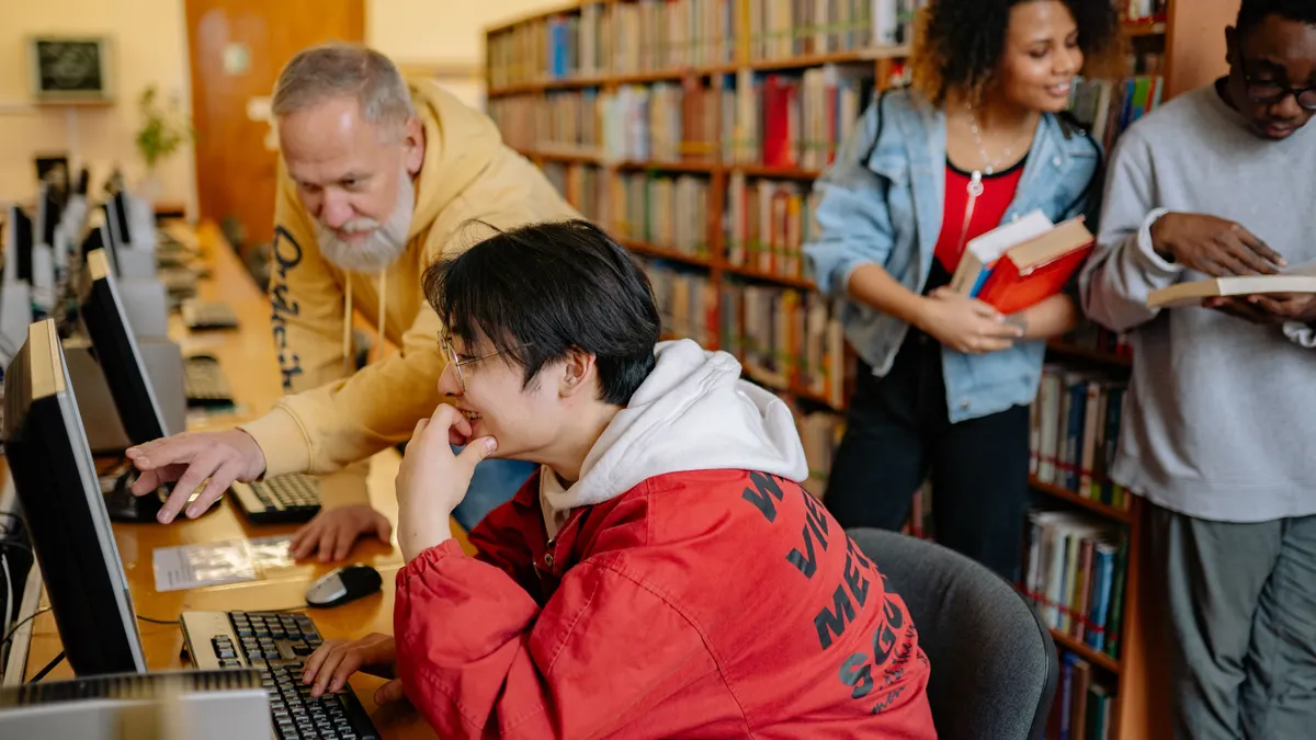 Students collaborating and learning in a library setting, engaging with computers and boo