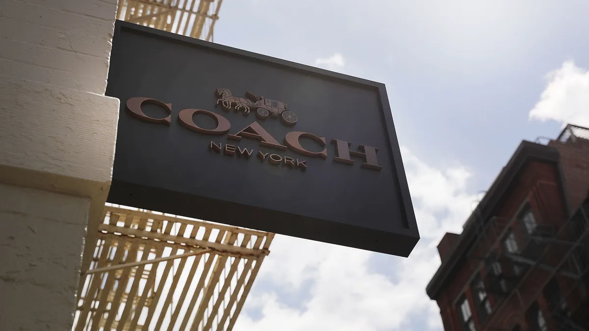 A sign reading "Coach New York" is pictured outside of a Coach storefront. The sign features the Coach logo, a horse drawn carriage.