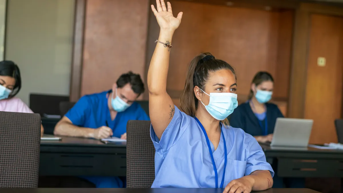 A female medical student attending a school lecture raises her hand to ask a question.