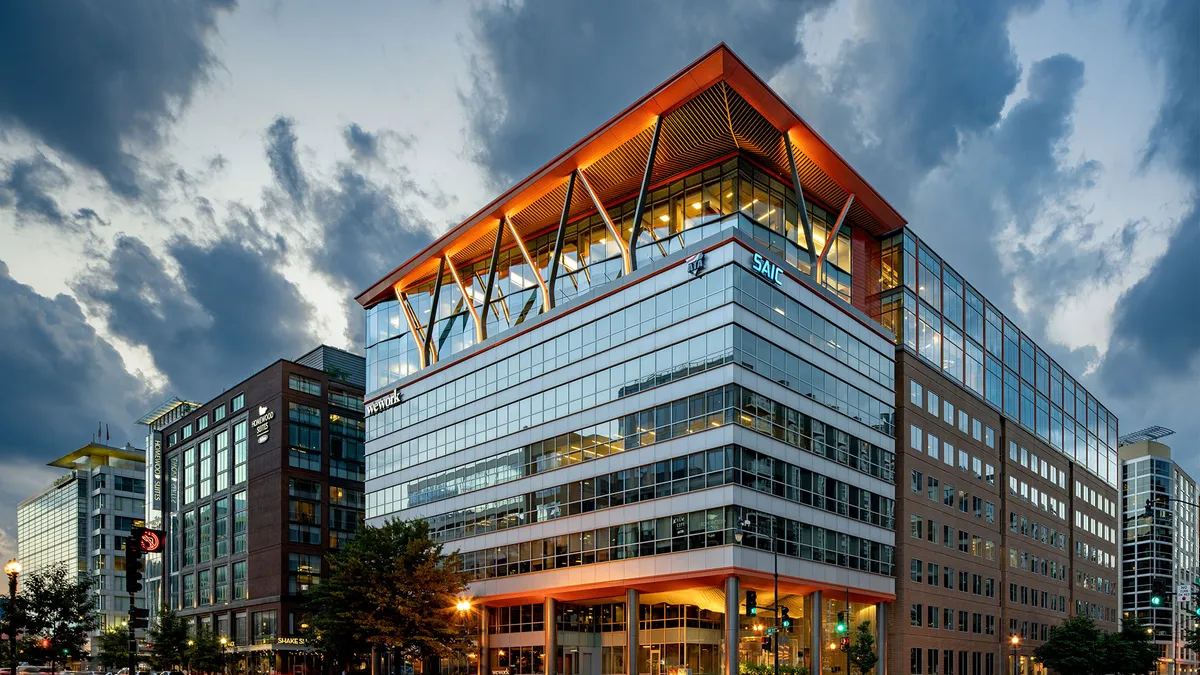 An exterior shot of a glass window-covered office building in SE Washington, D.C. The top floors feature angled architecture, and the building has a mass timber overbuild.