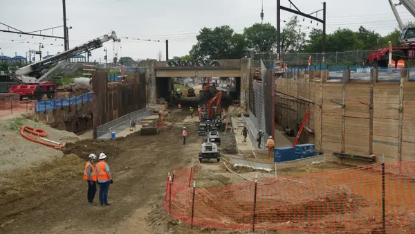 Construction crews and machinery on a jobsite around a bridge.