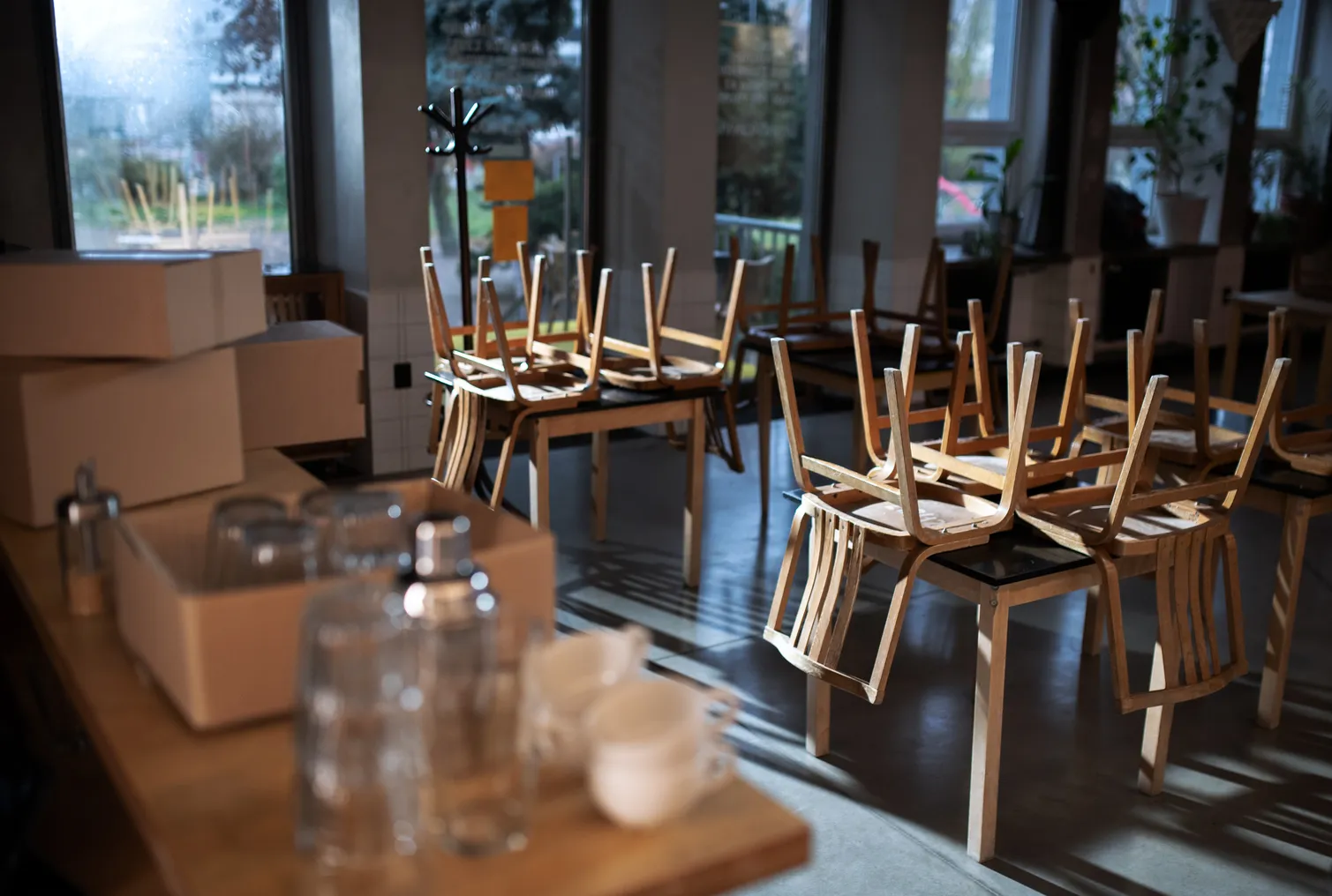 An empty, dark restaurant has chairs stacked on top of the tables.