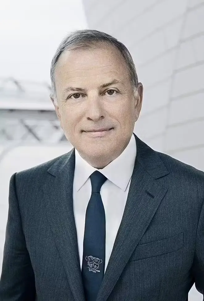 A corporate headshot features a man in a white shirt and a blue suit and tie.