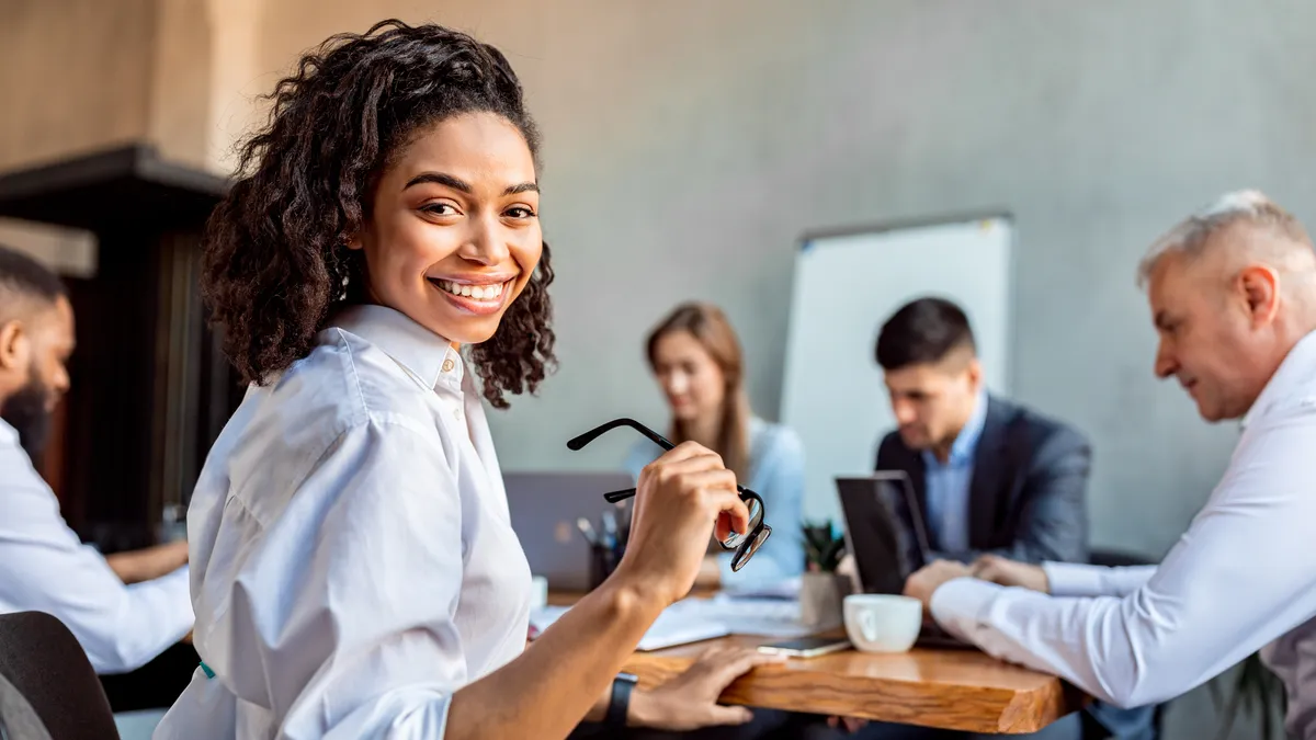 A person looking away and smiling while in a business meeting taking place in the background