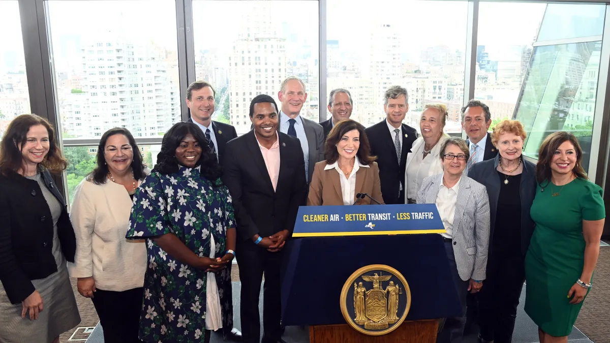 Surrounded by supporters, New York Gov. Kathy Hochul stands at a podium during a press conference.