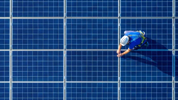 Engineer in blue suit and protective helmet installing photovoltaic panel system.