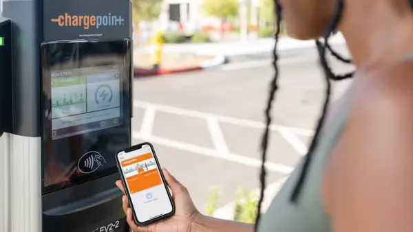 A person holds a smartphone at a public electric vehicle charger branded with the ChargePoint logo.