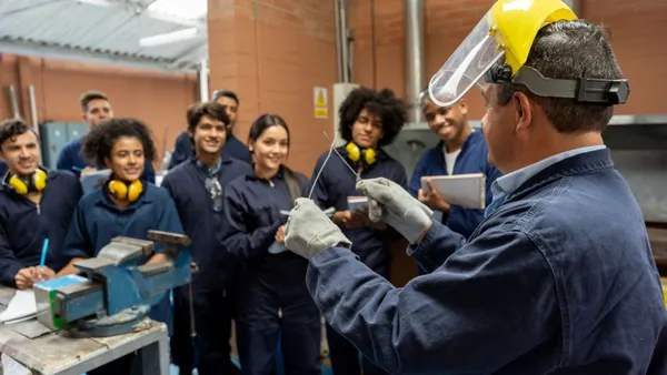 A group of students in overalls take instruction in a trade school class.